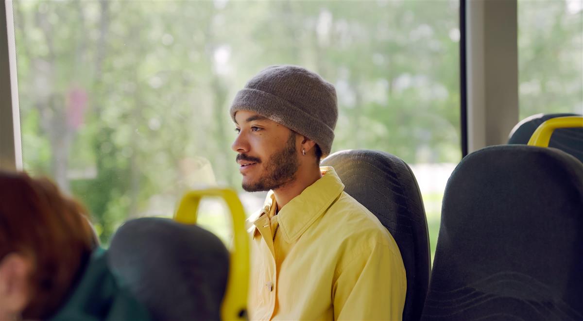 Bilde av en mann med lue og gul skjorte som sitter på bussen. - Klikk for stort bilde
