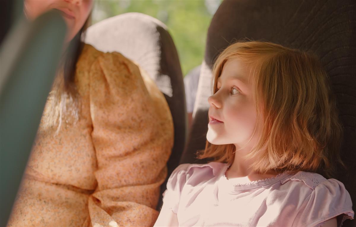 Ung jente sitter på bussen og ser ut gjennom vindu. Mor sitter ved siden av henne. - Klikk for stort bilde